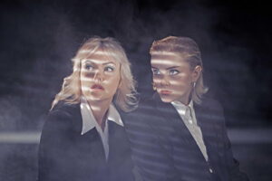 2 young women sitting in suits and shadows looking aside